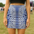 A high-waisted, bodycon mini skirt with a tight, fitted silhouette ending mid-thigh. The skirt features a vibrant, all-over graphic print inspired by a deer pelt. The pattern consists of a white and light blue textured base covered in irregular royal blue spots of varying sizes, creating a mesmerizing, psychedelic animal print effect. The skirt is made from a smooth, stretchy performance knit fabric with a subtle sheen, designed to hug the body's curves. The elastic waistband is seamless.